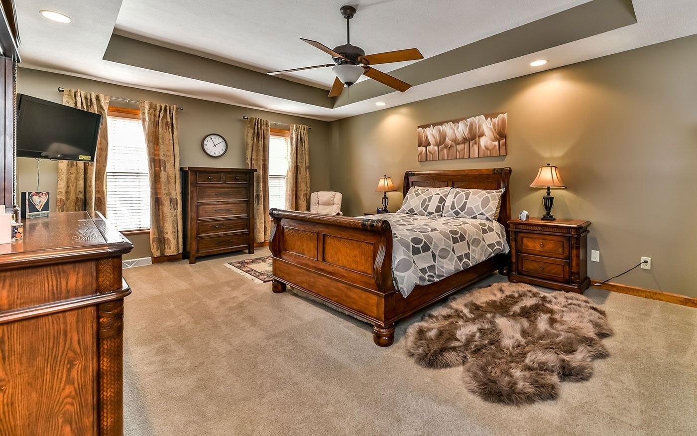 A bedroom with ornate wooden furniture, a large bed, and a fluffy rug, in warm tones.