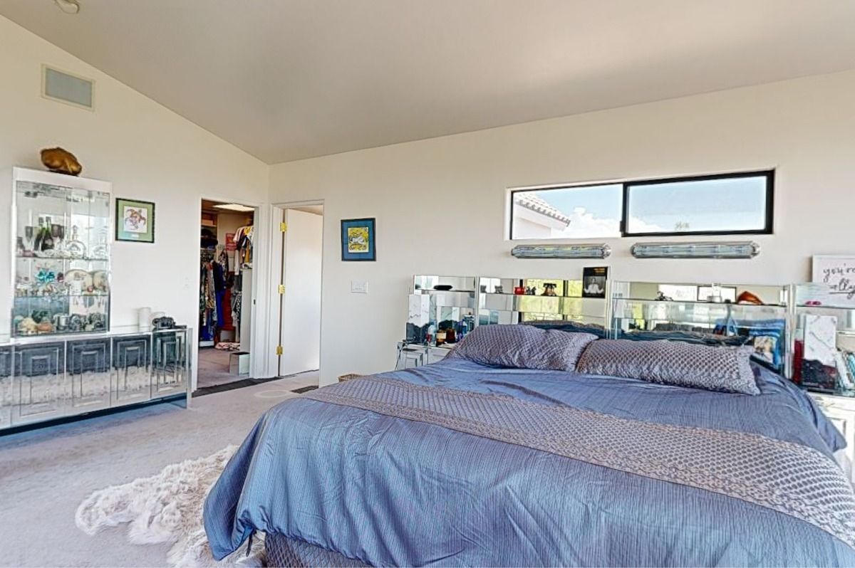 Spacious bedroom with a large bed, mirrored furniture, and a walk-in closet. Neutral colors dominate the space.