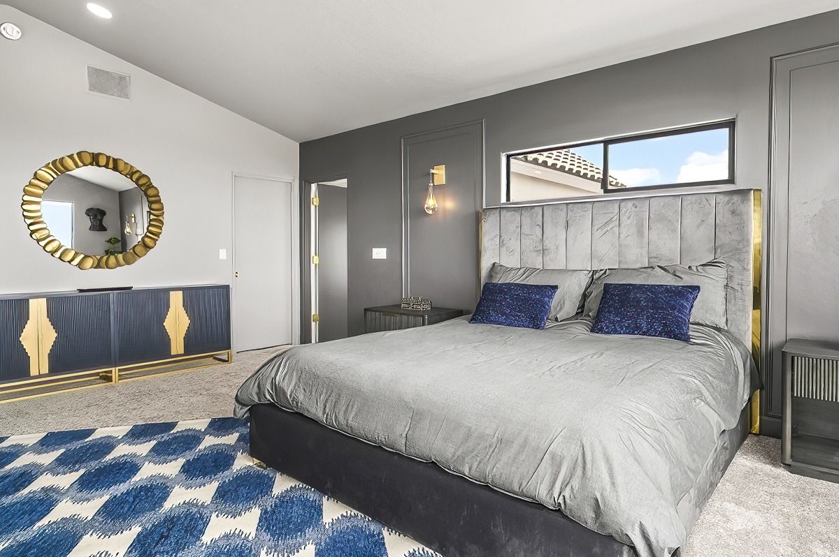 Bedroom with gray walls, bed, blue and gold accents, and a rug.