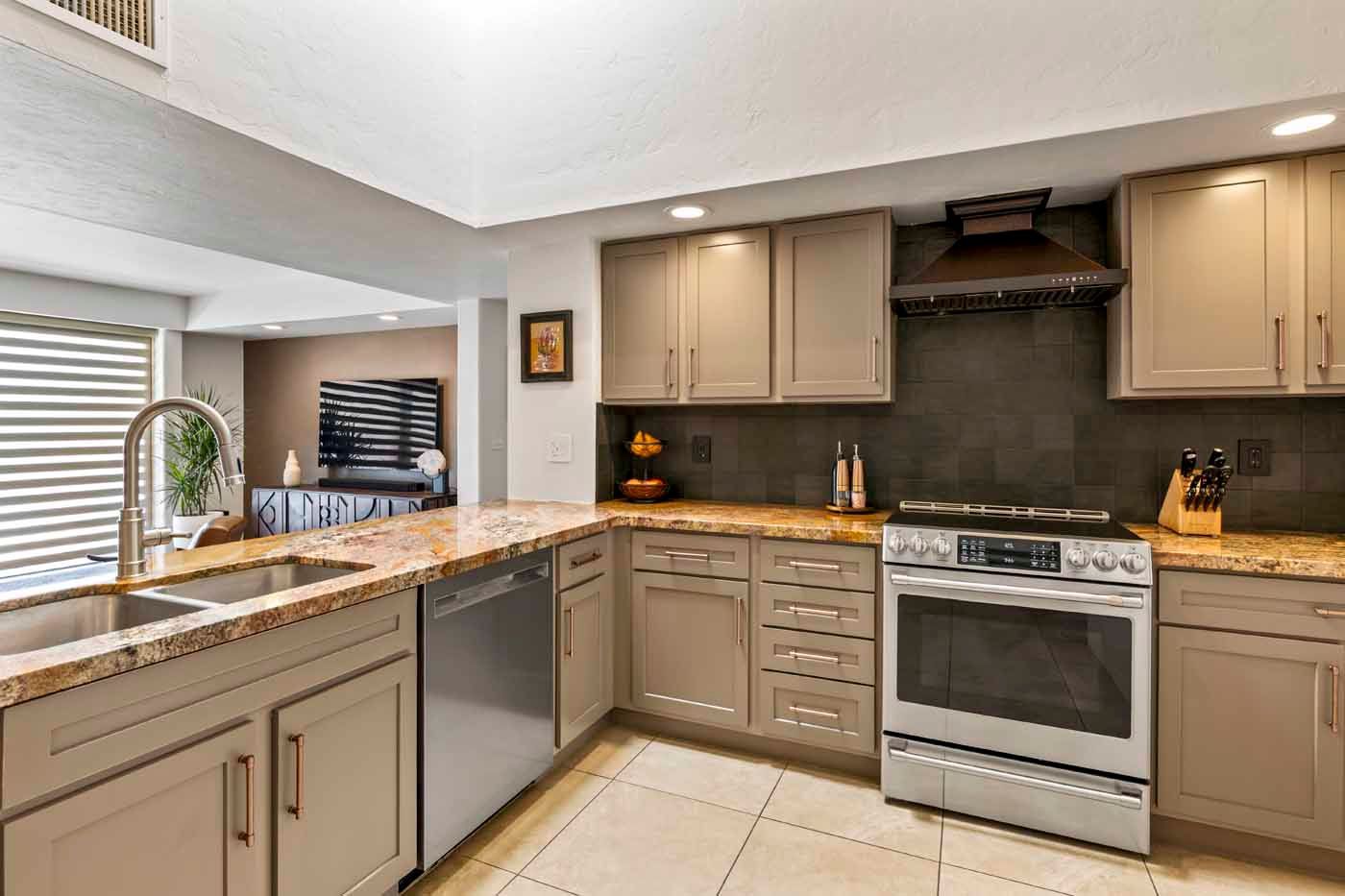 L-shaped kitchen with beige cabinets, stainless steel appliances, and granite countertops. View of adjacent living room.