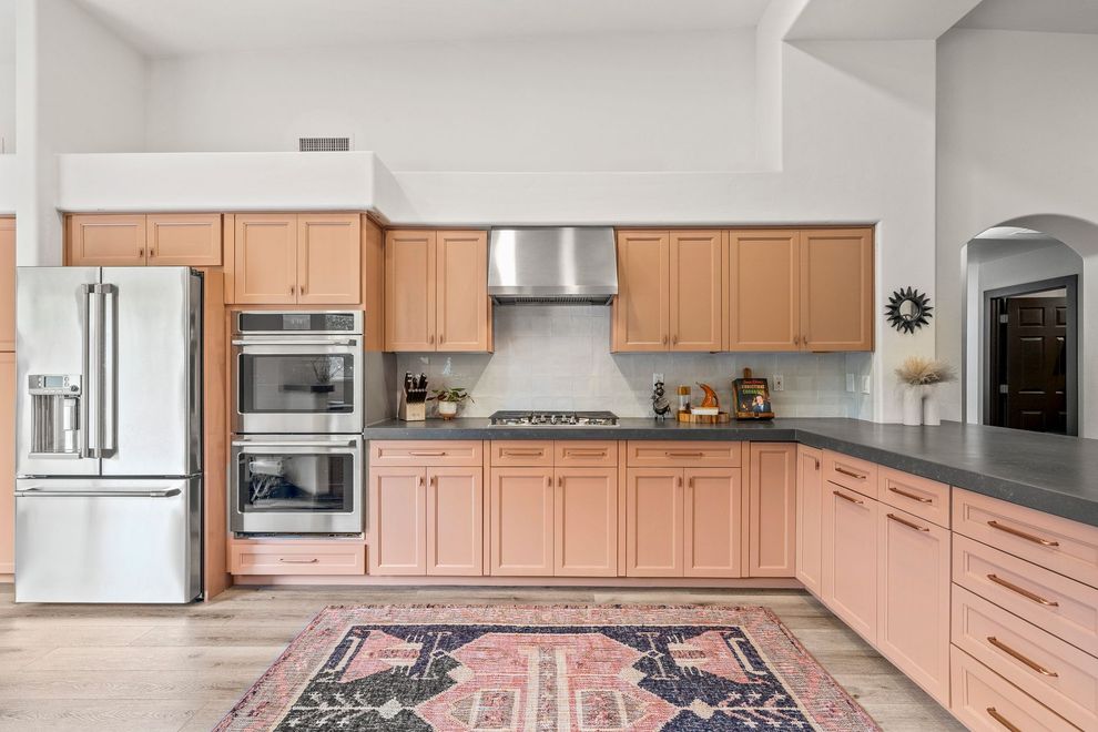 Peach-colored kitchen with stainless steel appliances, gray countertops, patterned rug, and arched doorway.