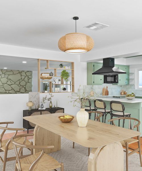 A modern dining room with a light wood table, woven chairs, and a pastel green kitchen.