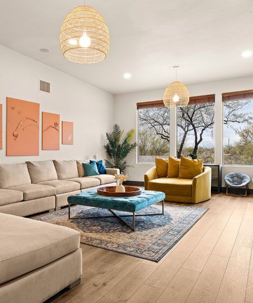 Modern living room with beige sofa, blue ottoman, yellow chair, and neutral wood floors.
