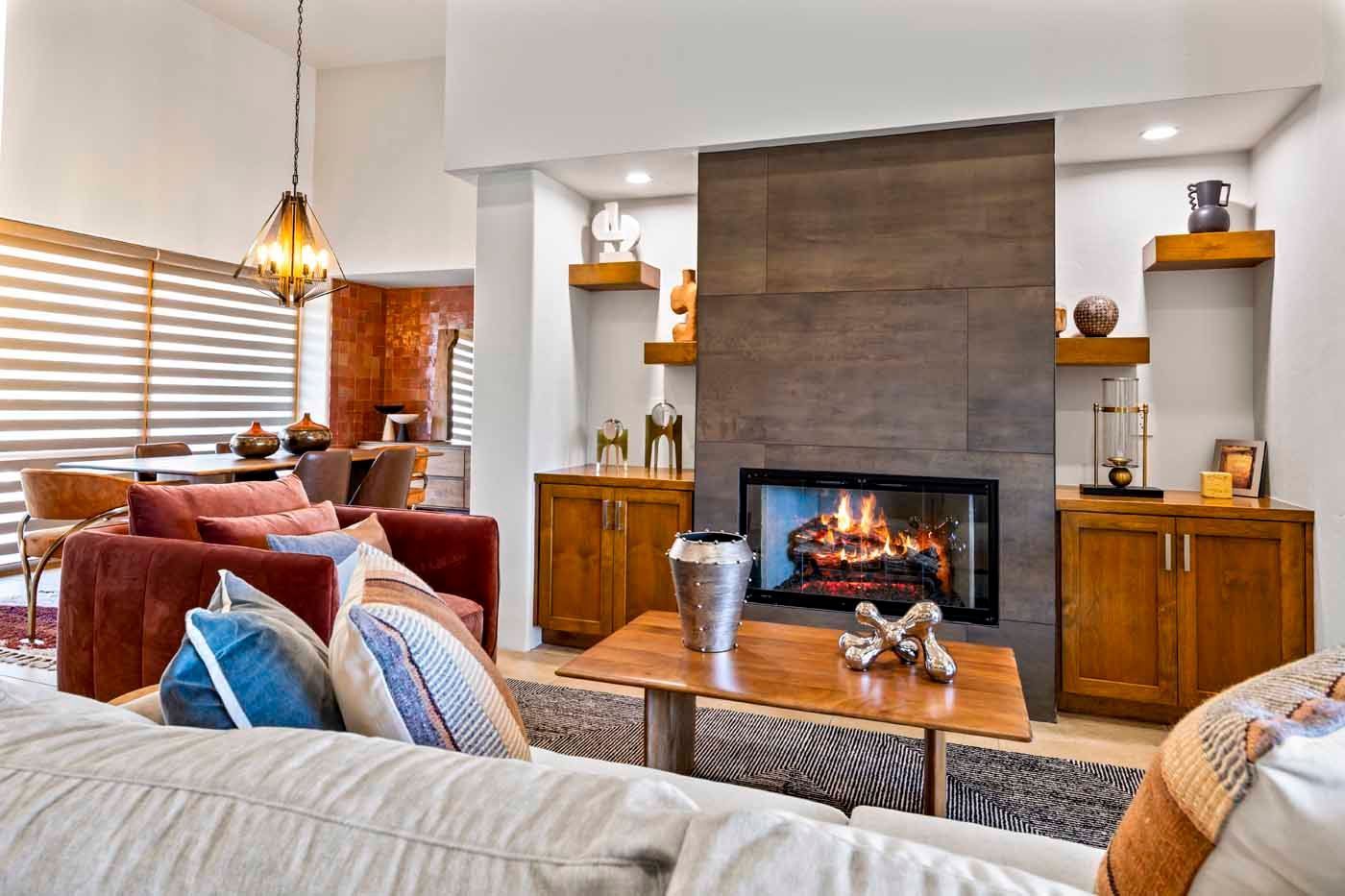 Living room with fireplace, wooden cabinets, floating shelves, and a sofa with colorful pillows.