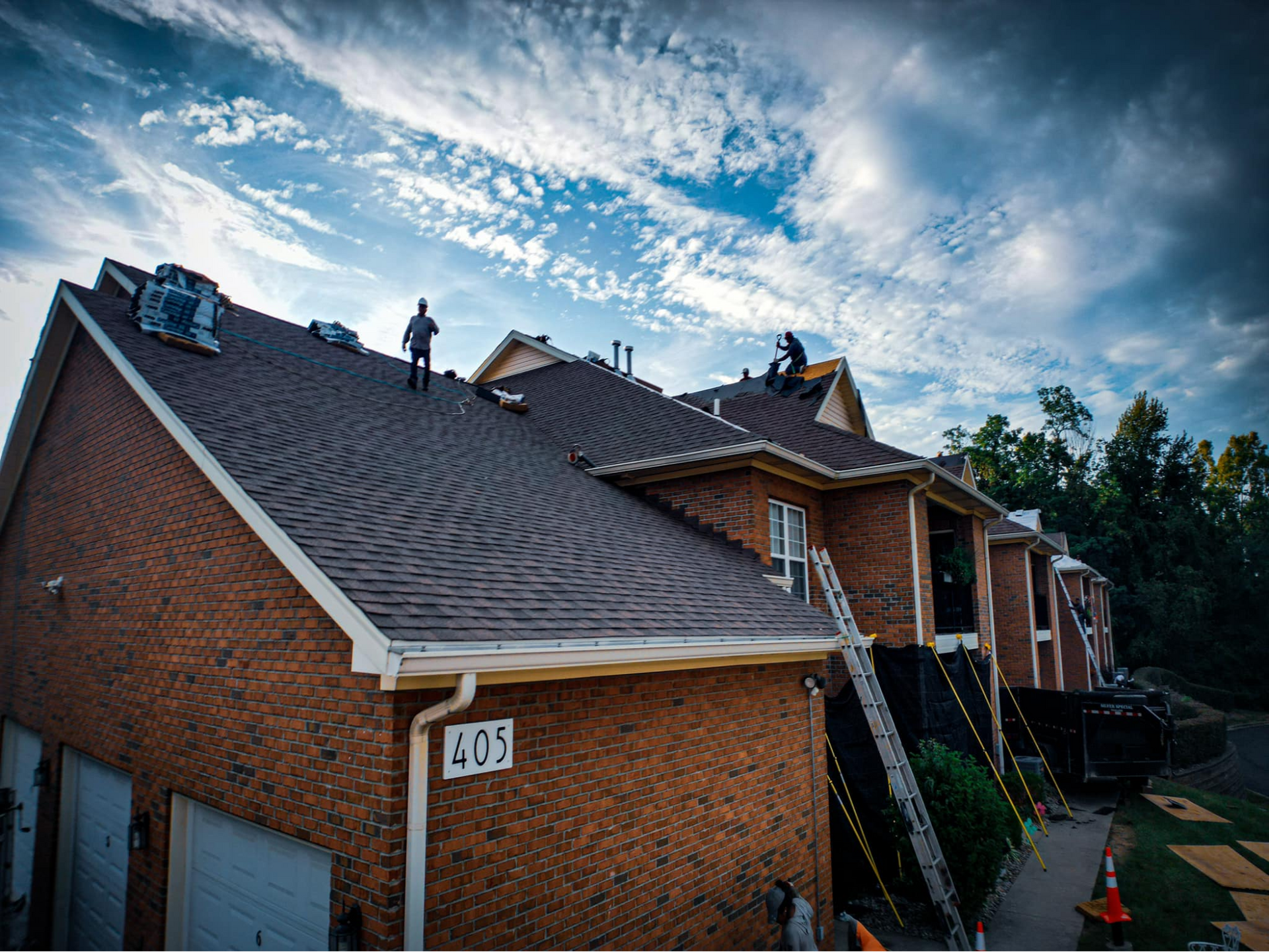 A group of people are working on the roof of a brick house.