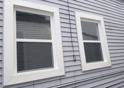 Two windows on the side of a house with white trim