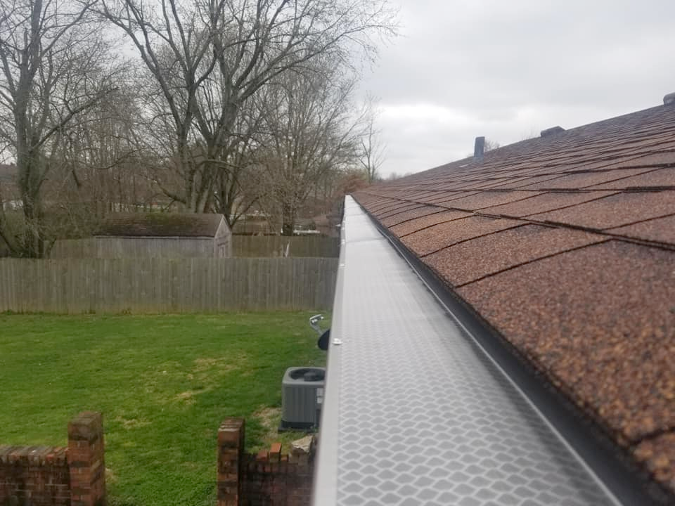 A gutter on the side of a house with a fence in the background.