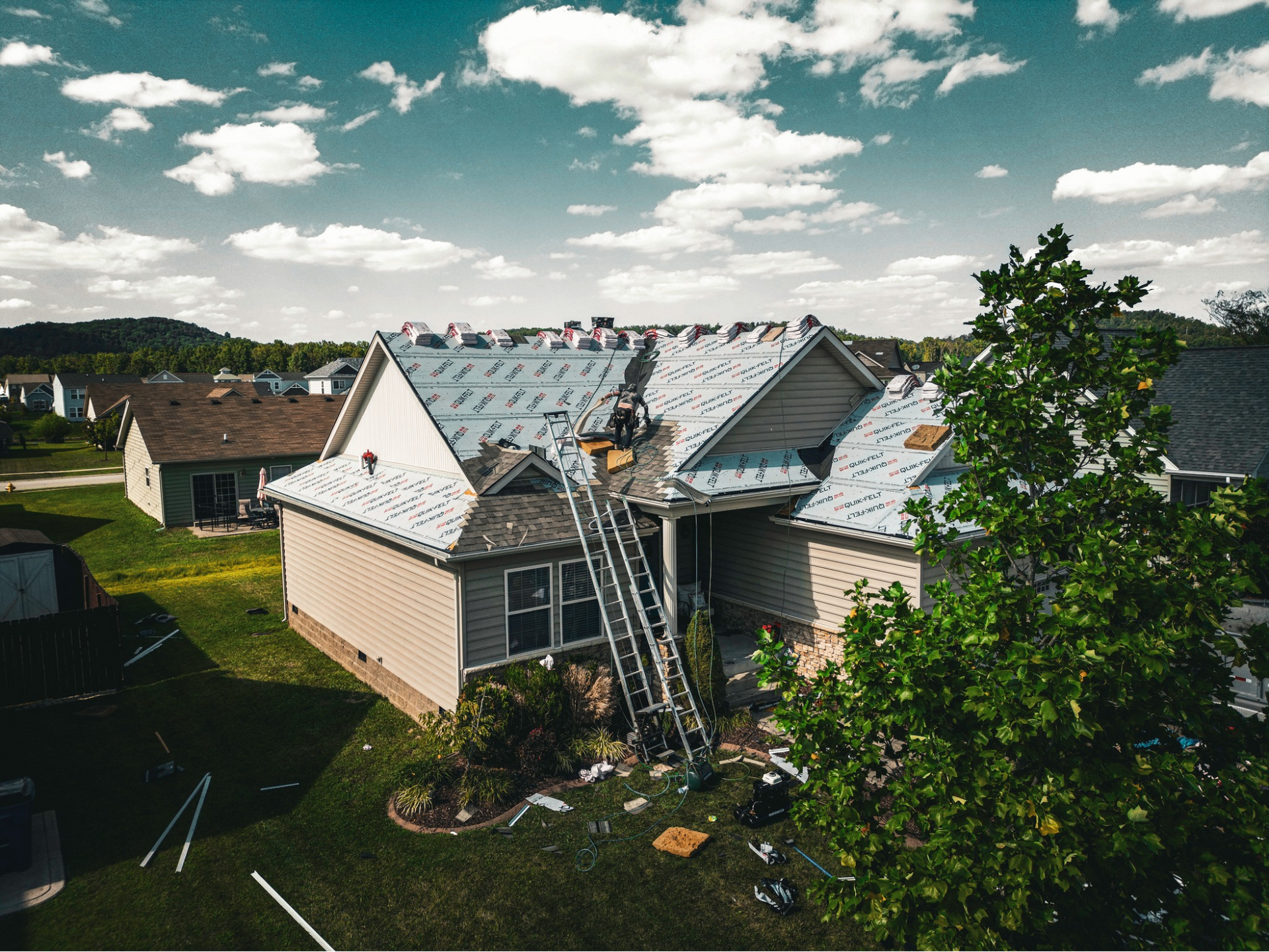 An aerial view of a house being remodeled with a ladder on the roof.