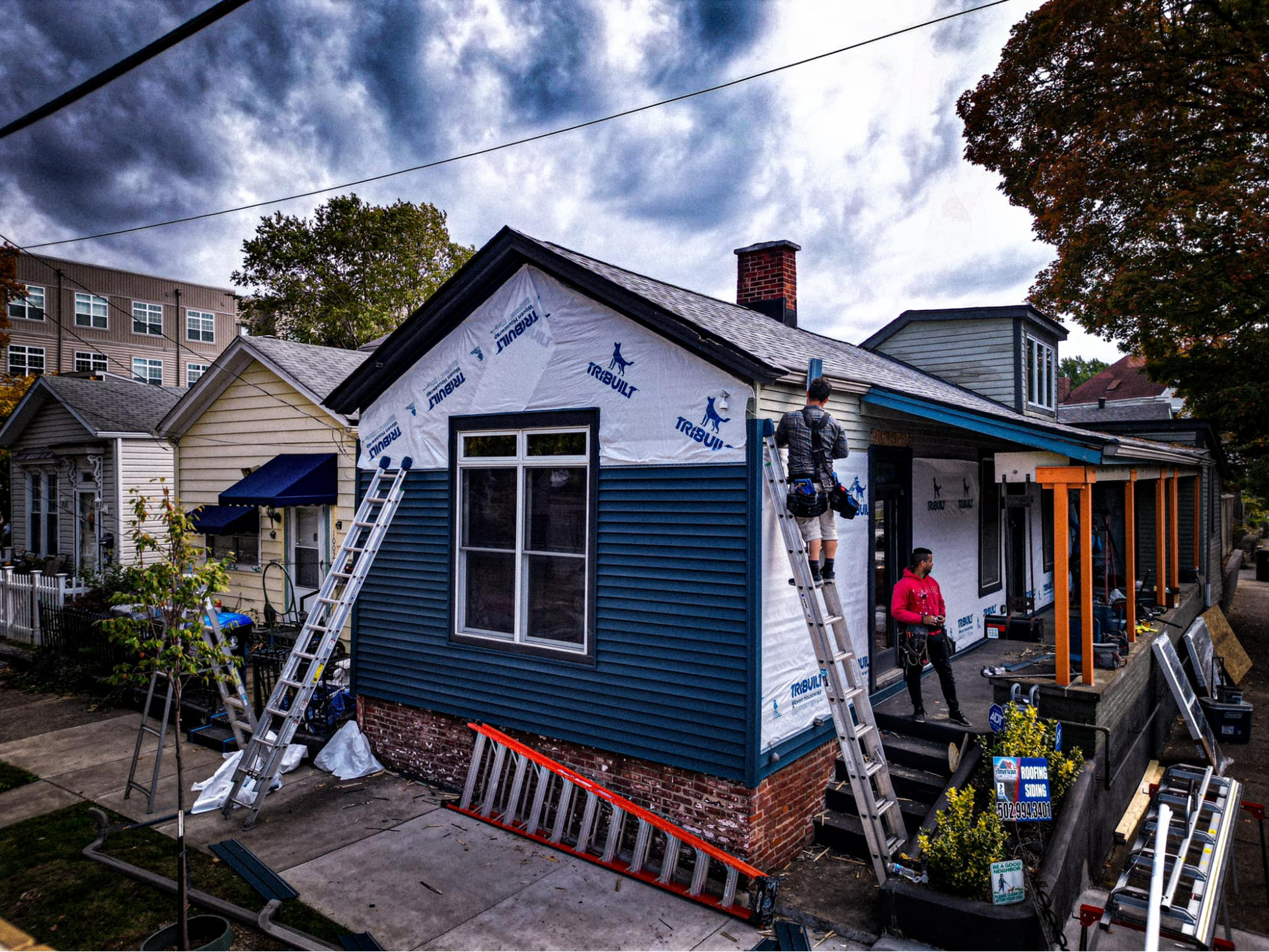 A man is standing on a ladder in front of a house being painted.