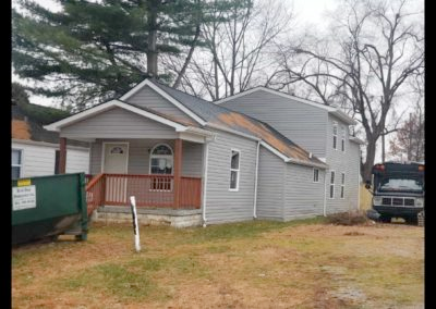 A house with a green dumpster in front of it.