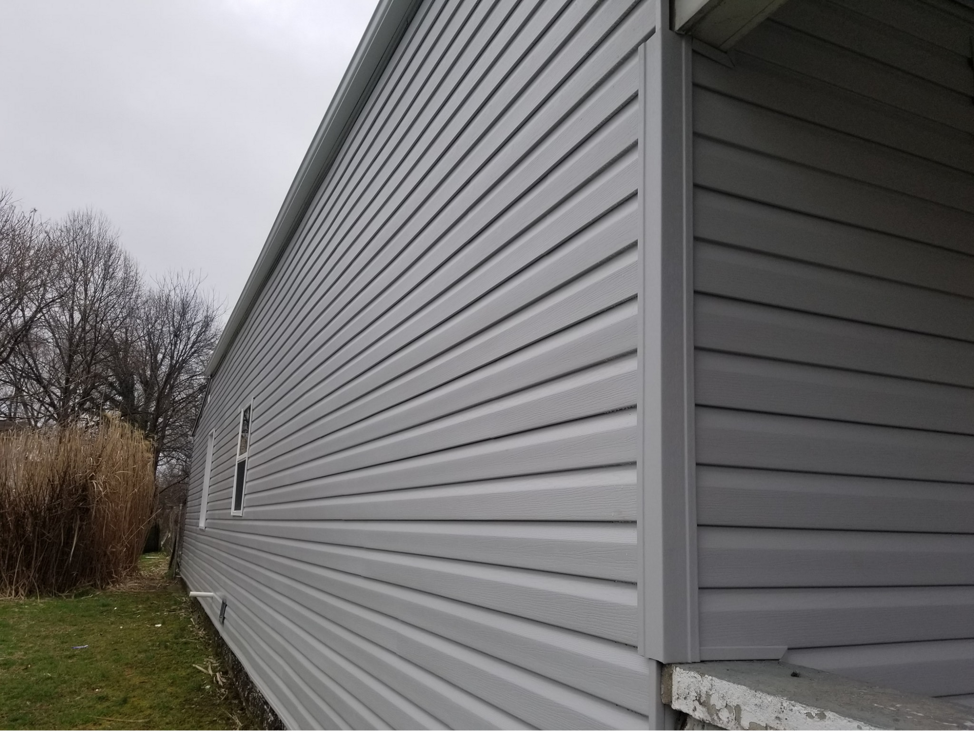 The side of a mobile home with white siding and a porch.