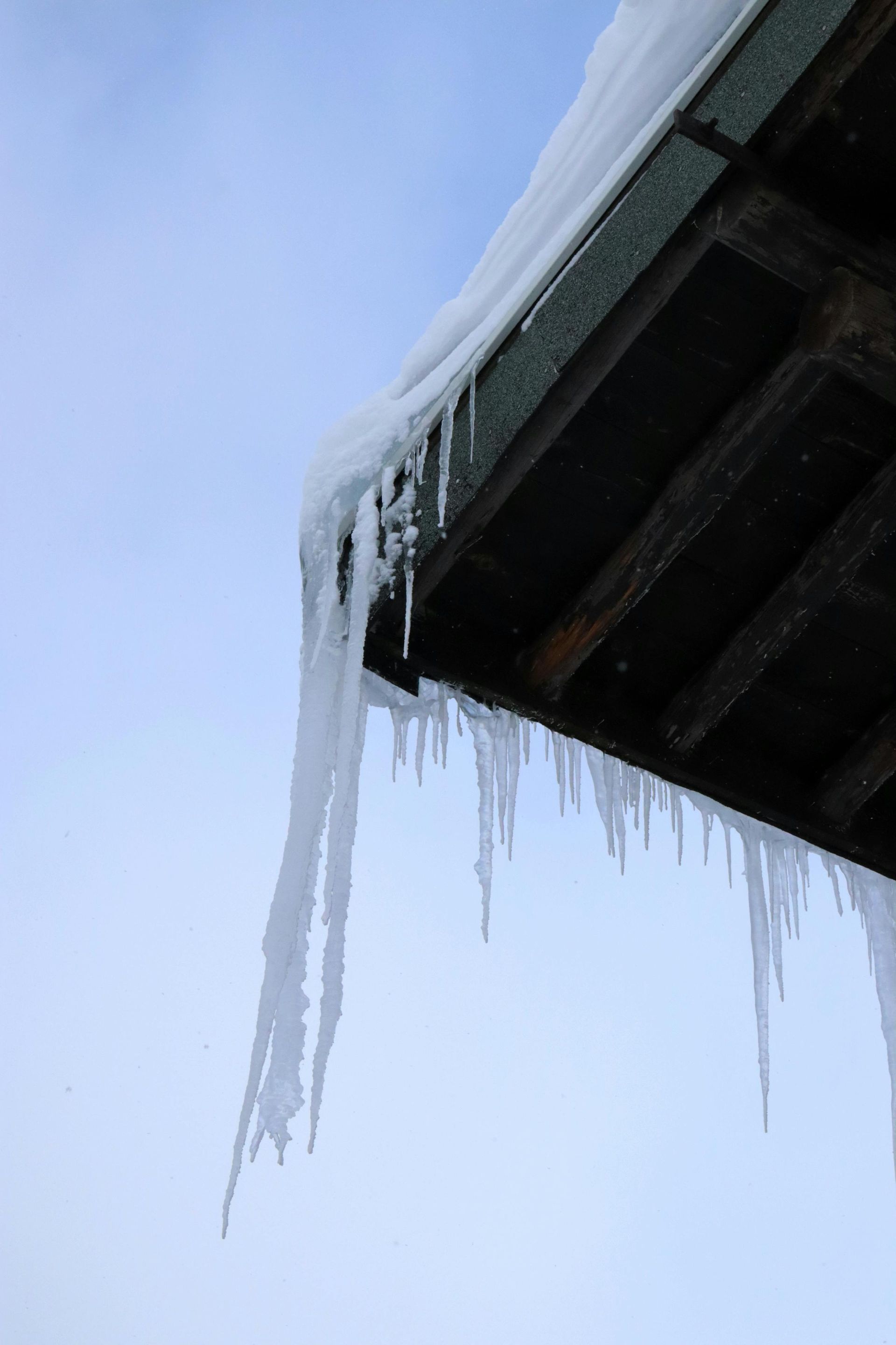 Icicles hanging from a roof's edge against a pale blue sky.