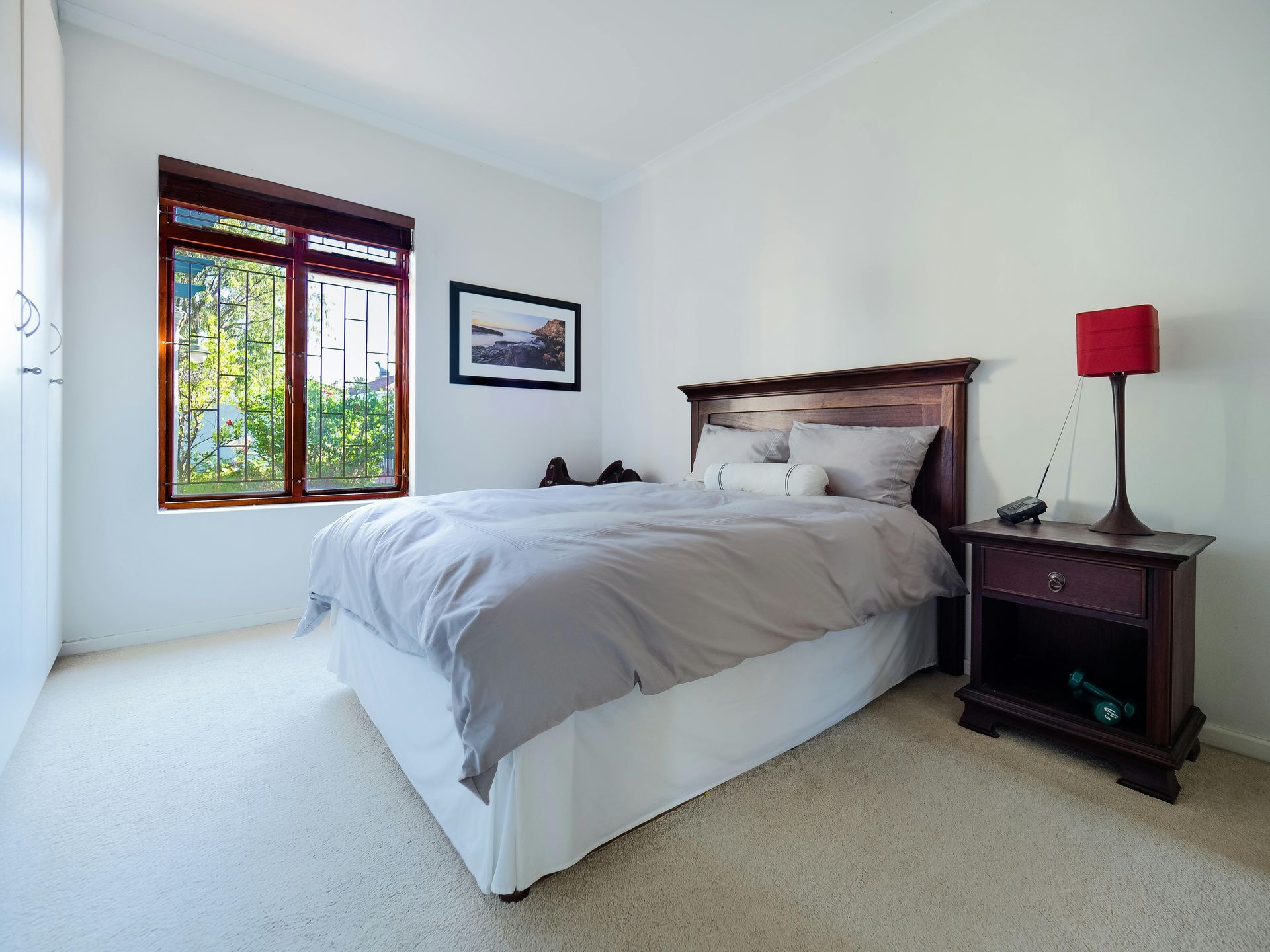 A bedroom with a bed , nightstand , lamp and double window.