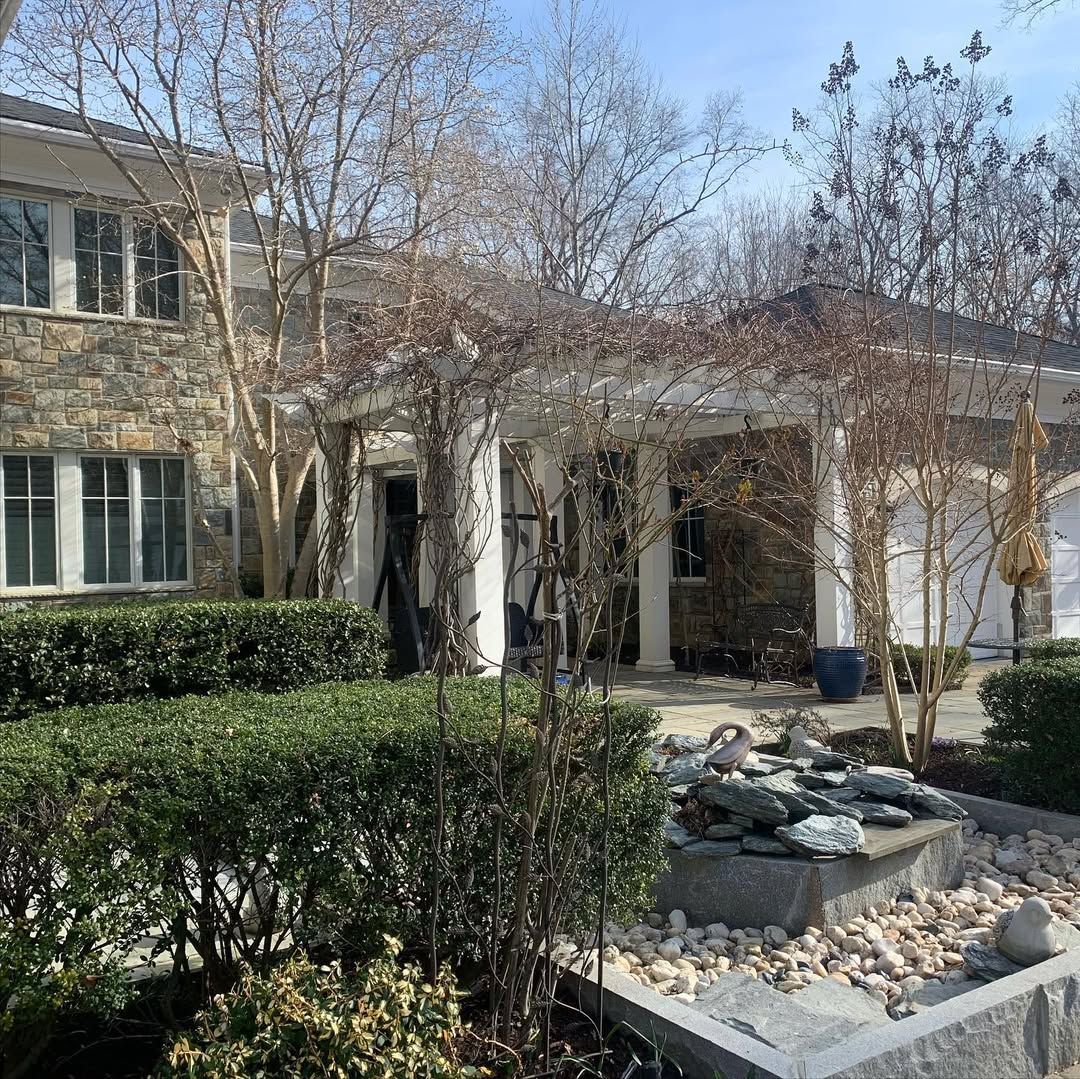 A stone retaining wall with vibrant pink roses growing above it and greenery tucked between the textured rock layers.