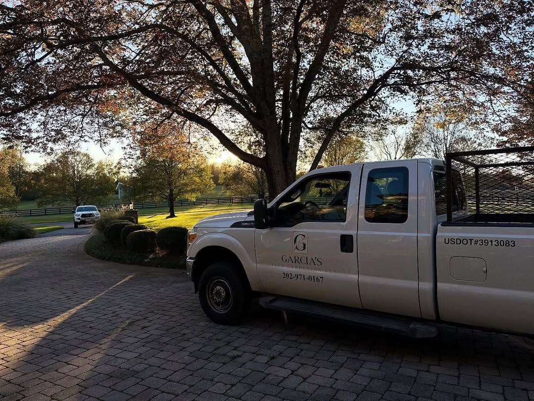 A white work truck parked on a cobblestone driveway under large trees at sunset.