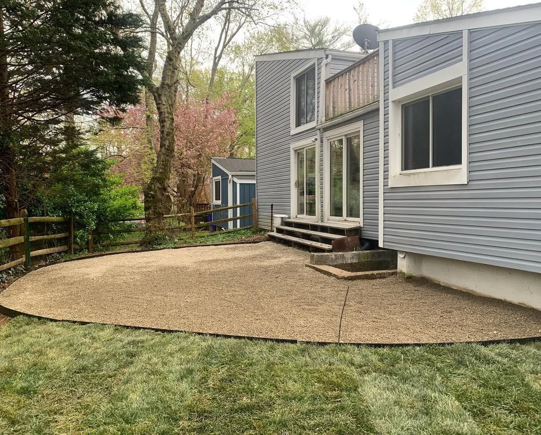 A light blue house with a gravel patio and stairs leading to sliding glass doors in a yard with trees.