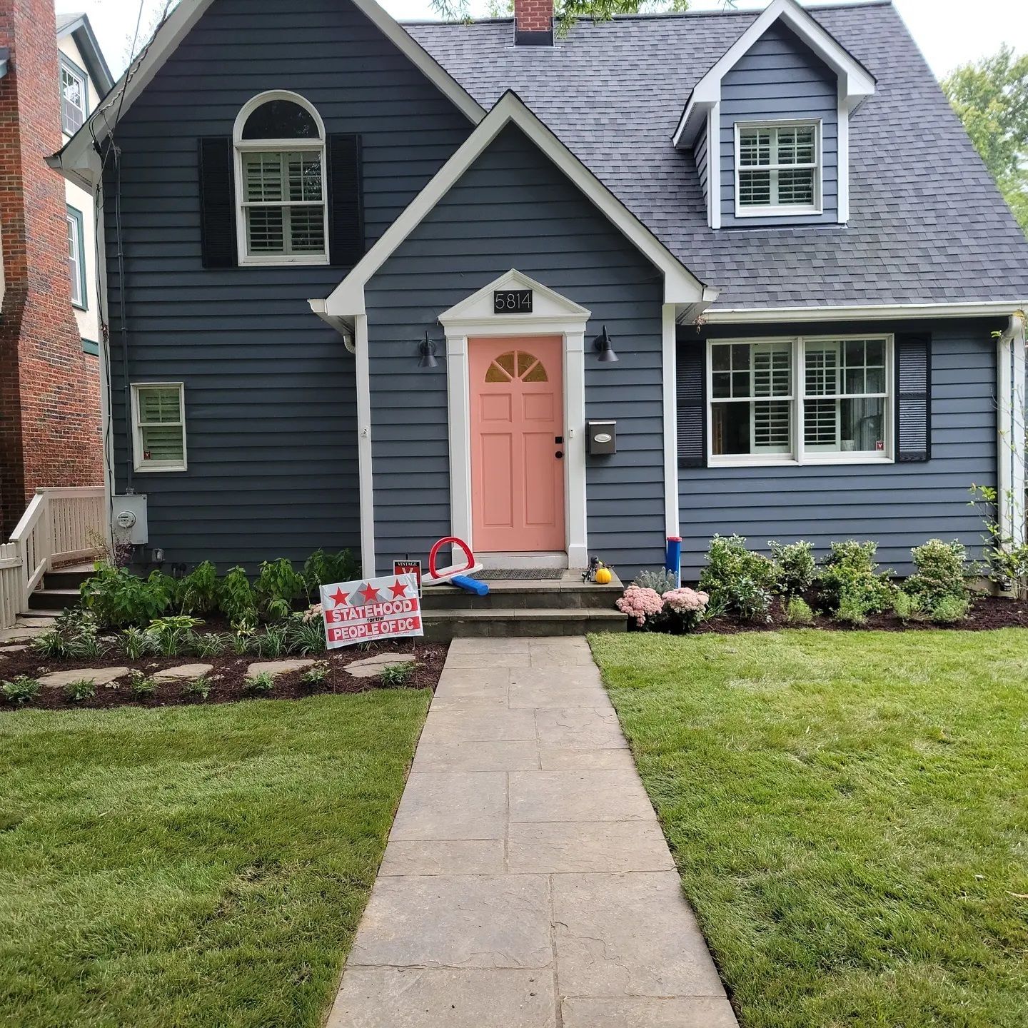A two-story dark blue house with a peach front door, a light gray stone walkway, and a landscaped front yard.