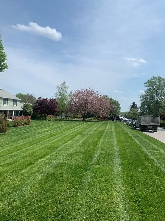 A manicured lawn with a flowering cherry tree and red-leafed tree in front of a house, with a truck parked on the side.