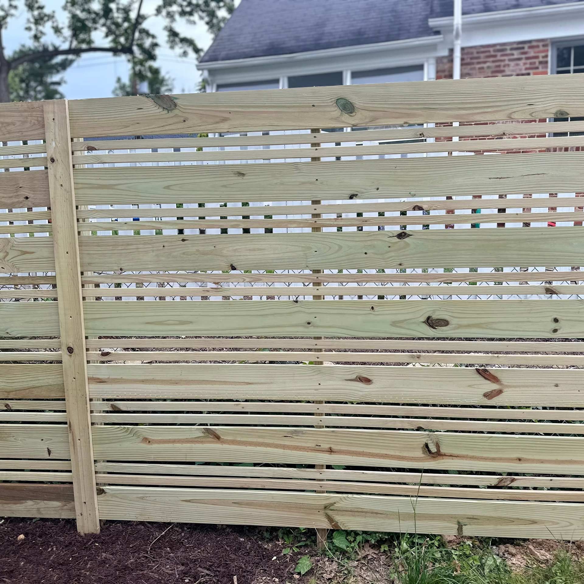 A newly installed wooden horizontal slat fence with alternating wide and thin boards set in a grassy yard.