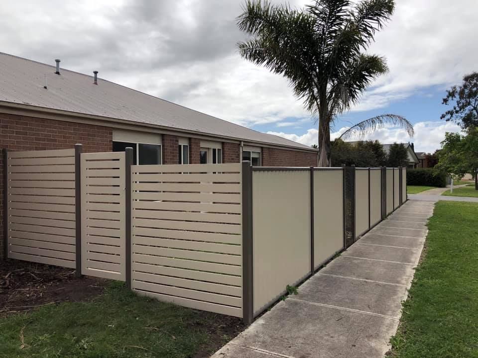 A fence along a sidewalk next to a house with a palm tree in the background.