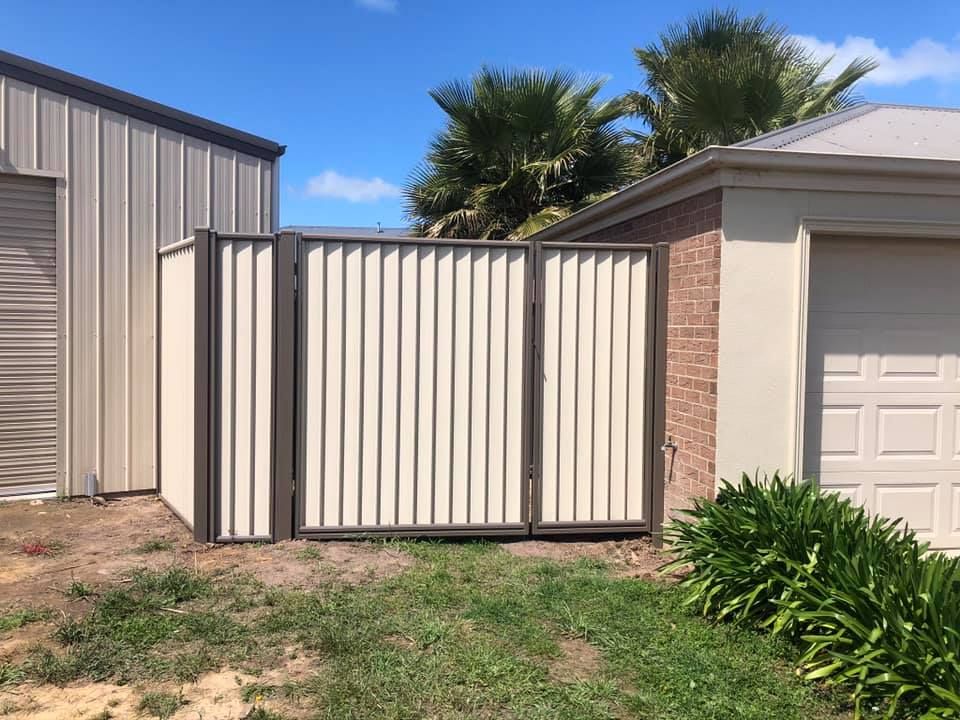 A white fence is sitting in front of a garage next to a brick building.