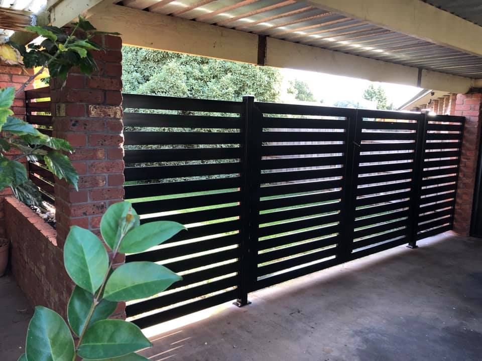 A black fence is sitting next to a brick wall.