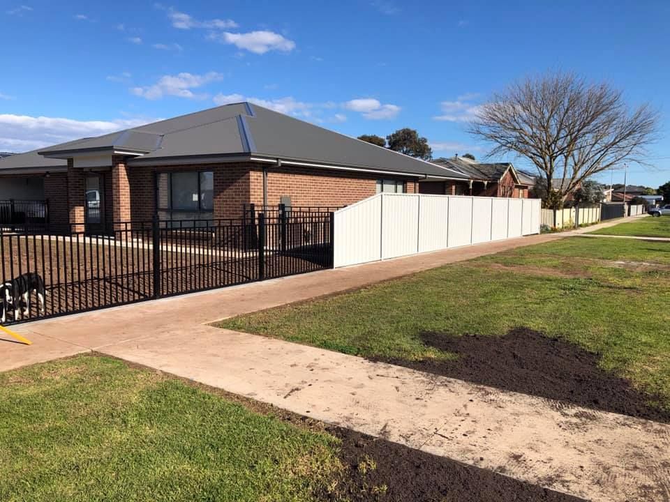 A dog is standing in front of a fence next to a house.