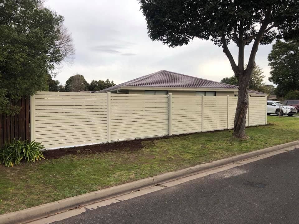 A white fence surrounds a house with a tree in front of it.
