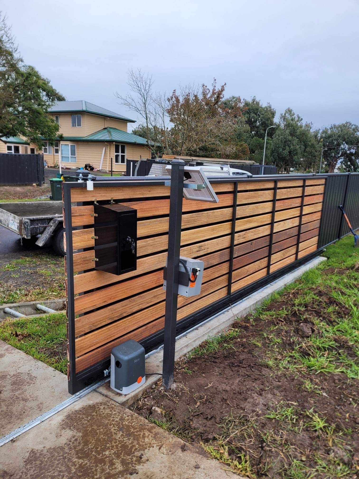 A wooden fence with a sliding gate and a mailbox attached to it.