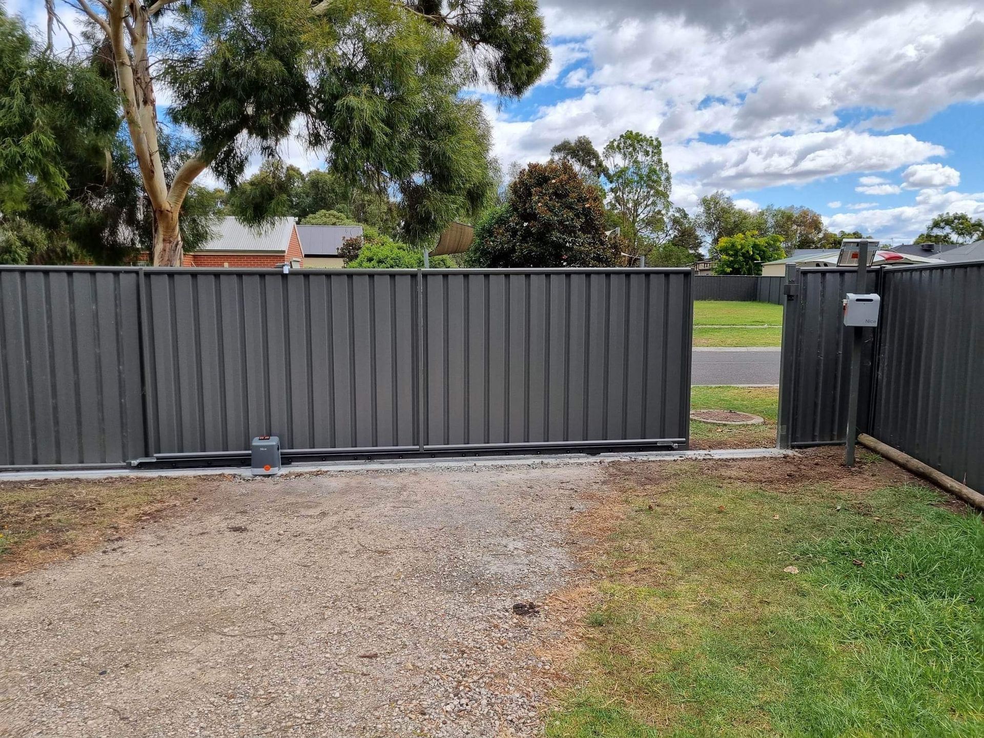 A sliding gate is open to a gravel driveway.