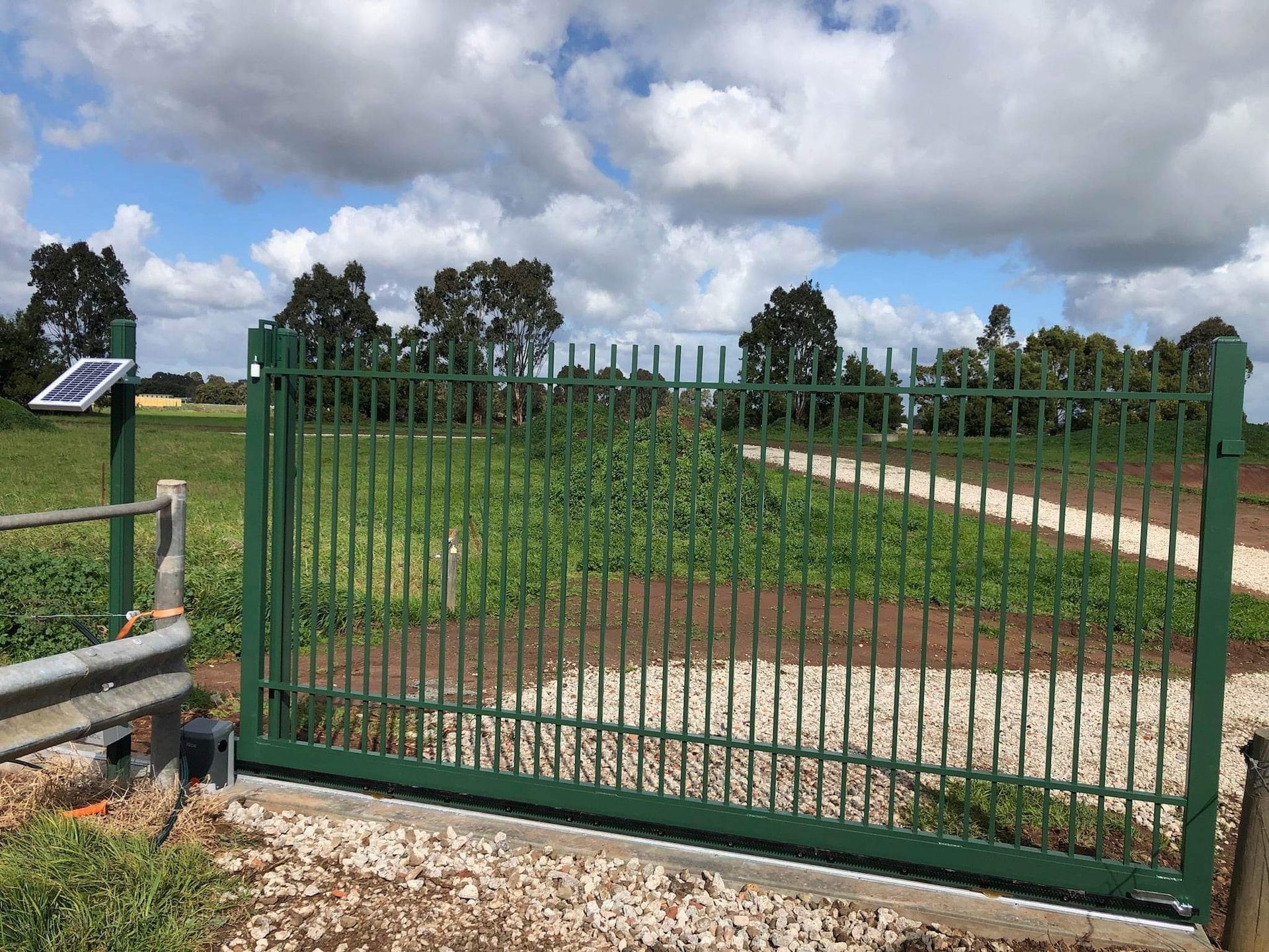 A green sliding gate with a solar panel on top of it.