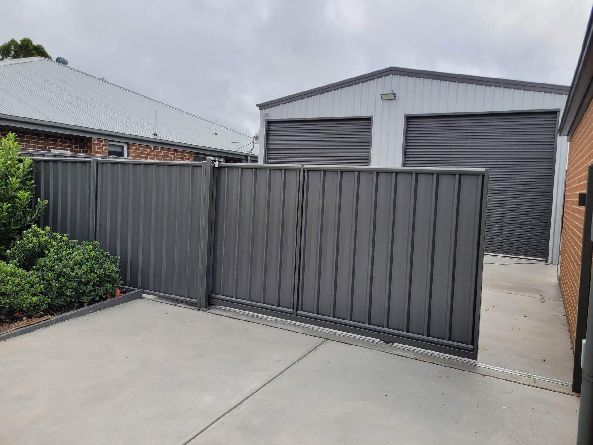 A garage with a sliding gate and a fence in front of it.