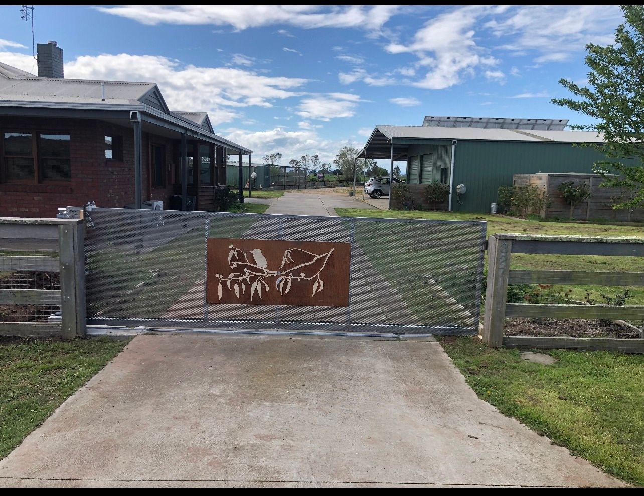 A sliding gate with a sign on it is leading to a house.