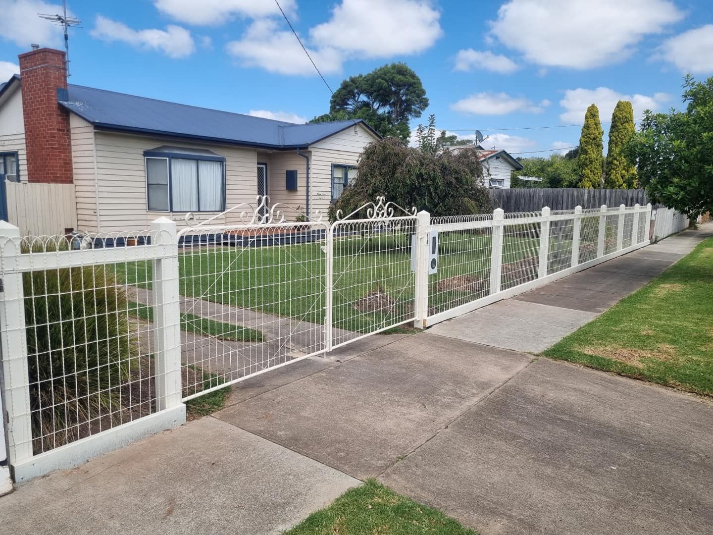 A white fence surrounds a house on a sunny day