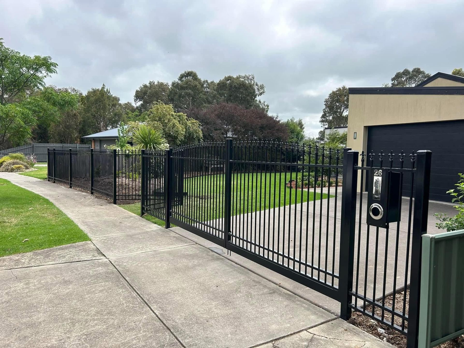 A black metal fence surrounds a driveway in front of a house.