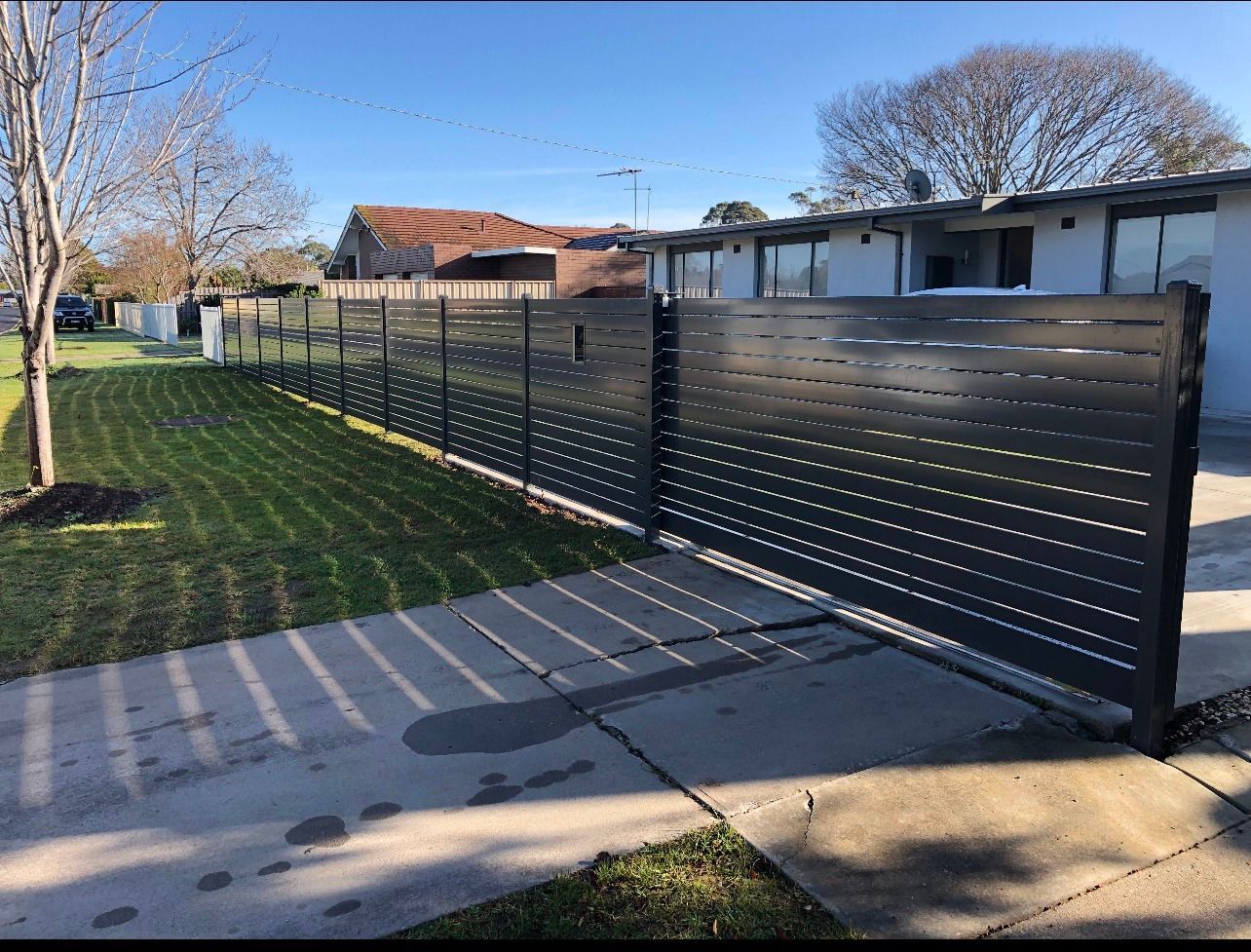 A black fence surrounds a lush green yard in front of a house.