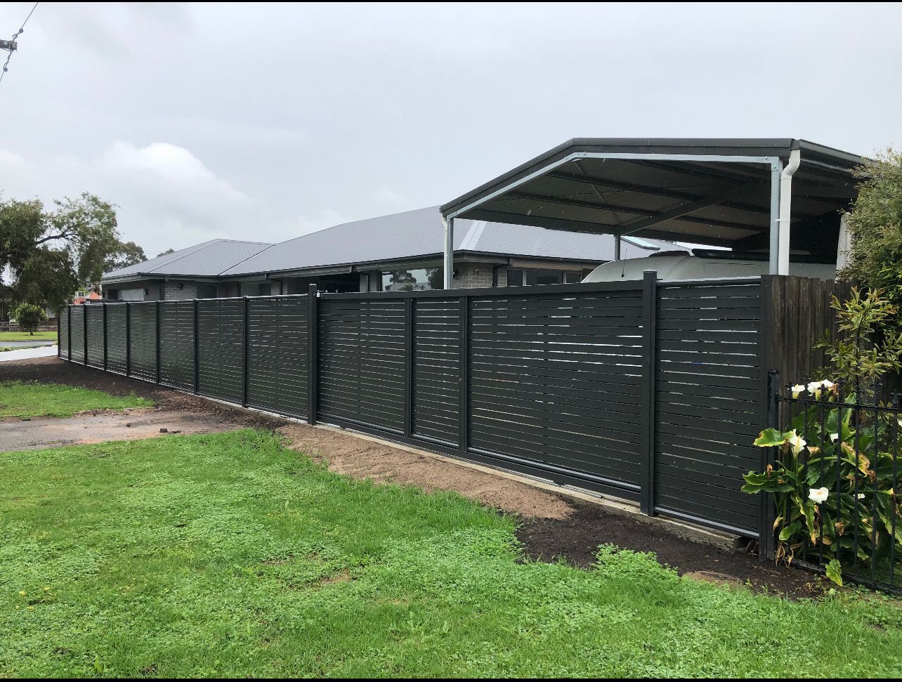 A fence with a carport in the background and a house in the background.