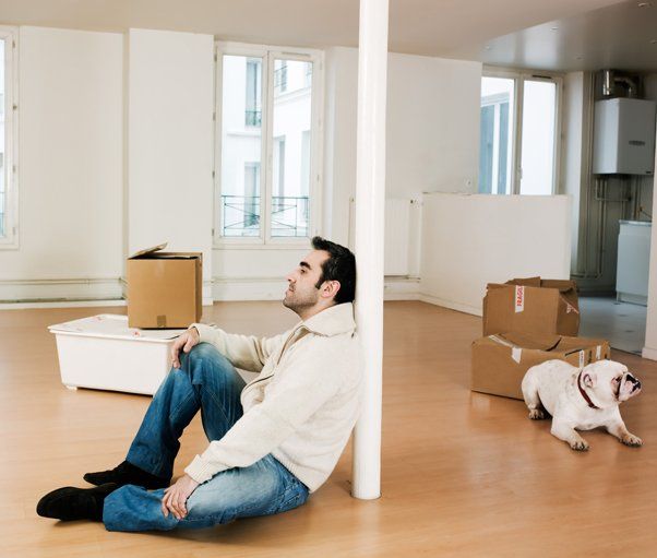 A man sitting in a room with a dog and packed boxes after selling his home