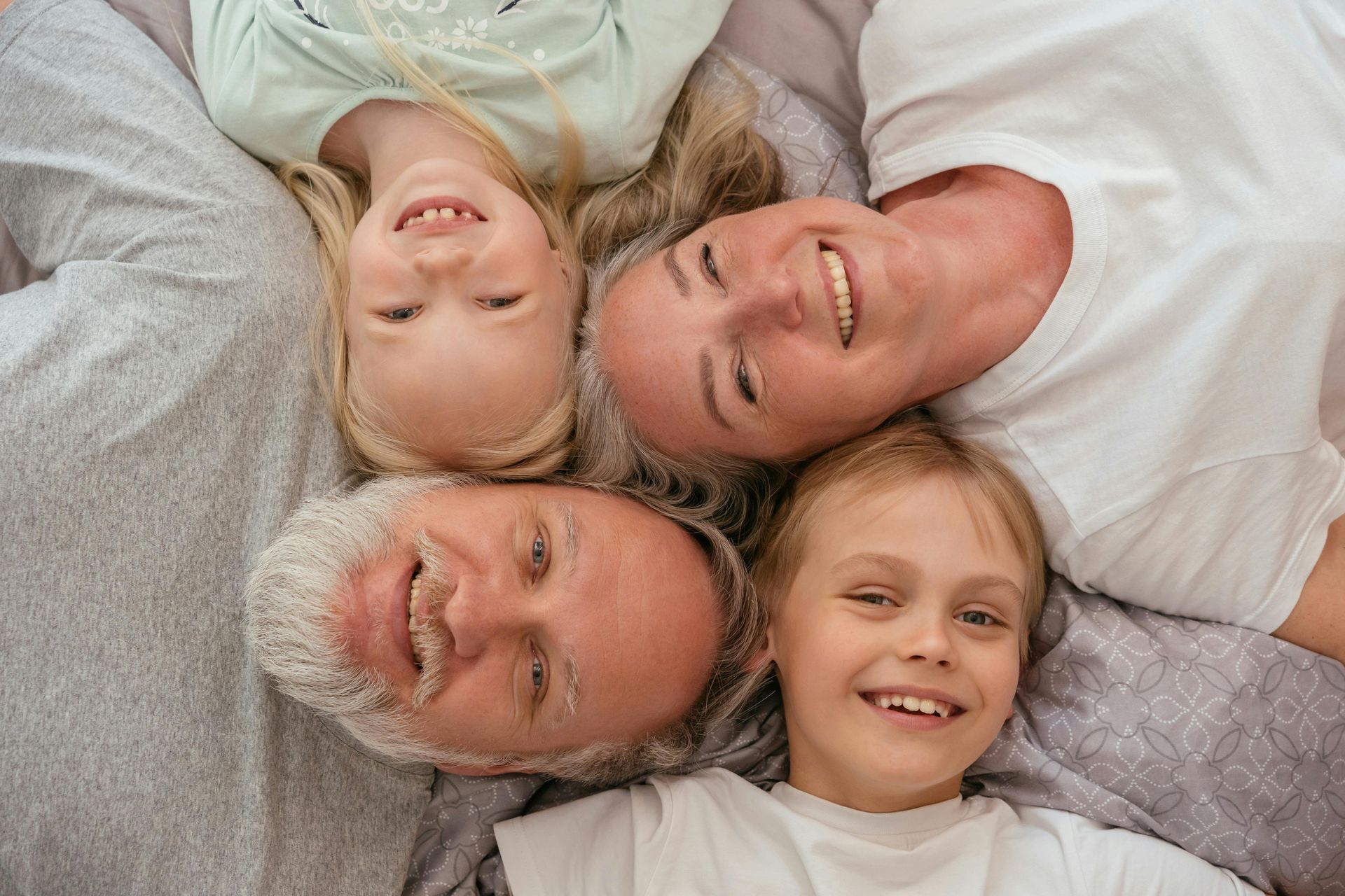A family is laying on a bed with their heads together and smiling.