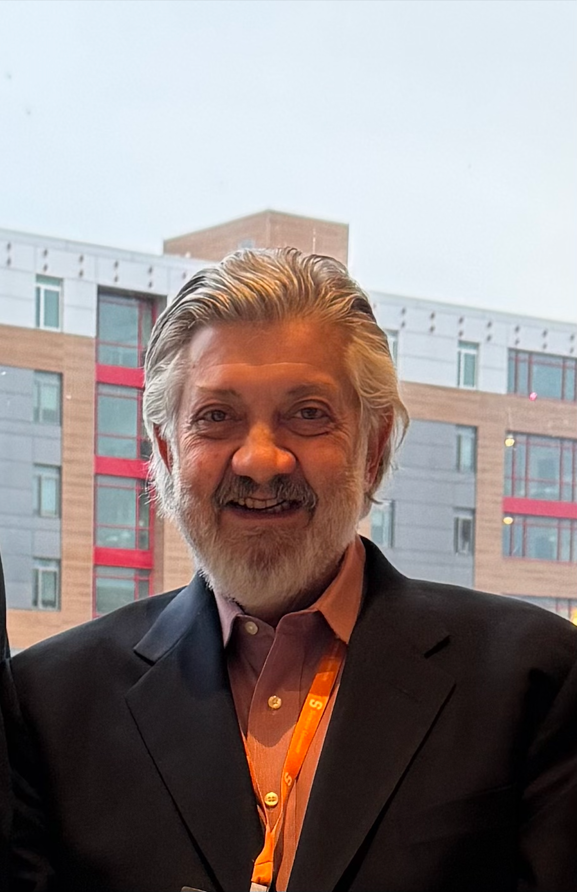 A man with a beard is smiling in front of a building