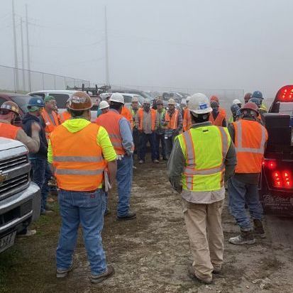 A group of construction workers are standing in a parking lot.