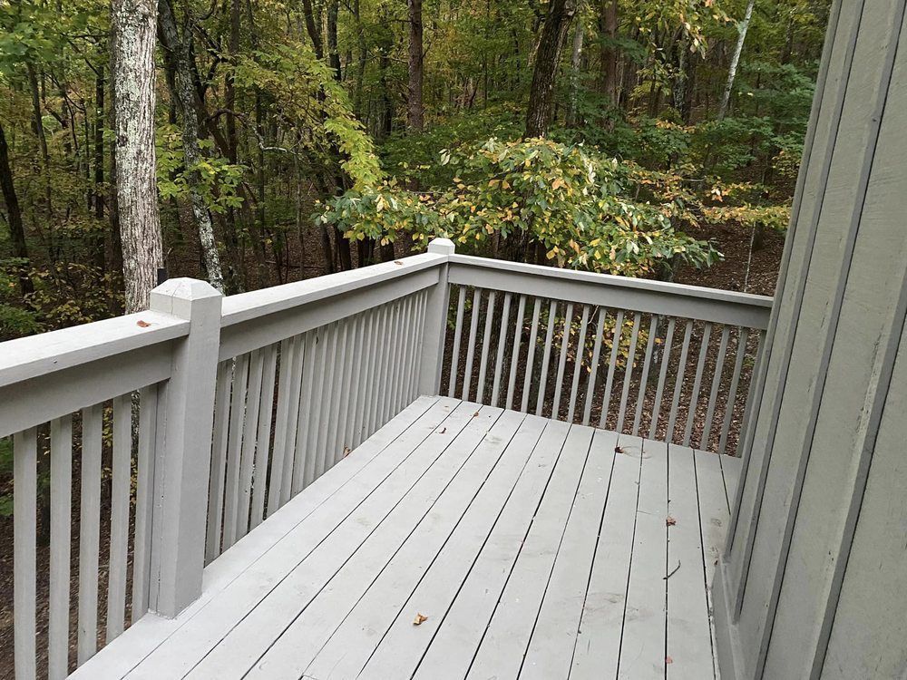 Wooden deck painted light gray overlooks a wooded area with green and yellow foliage.