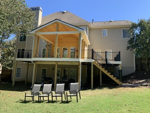 Back of a two-story house with a newly built covered deck, stairs, and black railings.