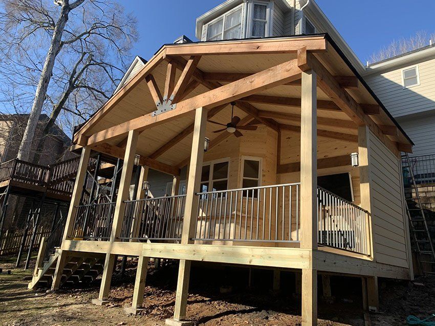 Wooden porch addition on a house with a light-colored exterior, featuring a gable roof, railing, and a deck.