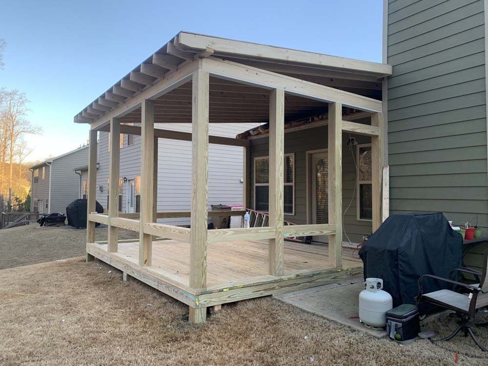 Unfinished wooden screened porch addition attached to a house.  A grill, propane tank, and chair are visible.