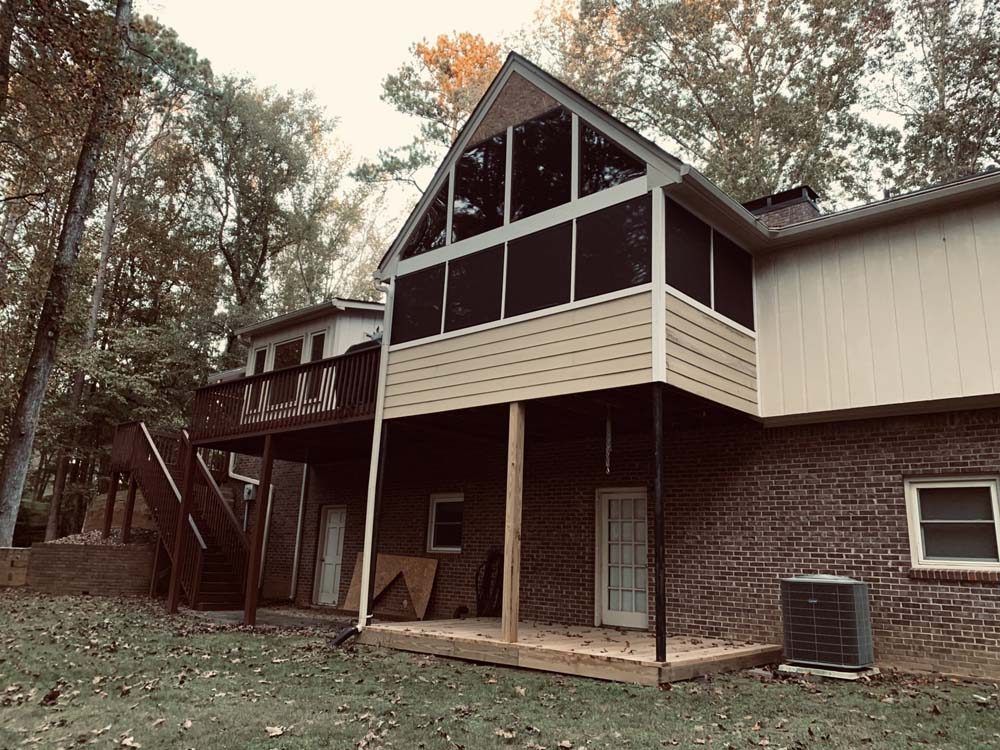 Screened-in porch and deck attached to a brick house with trees in the background.