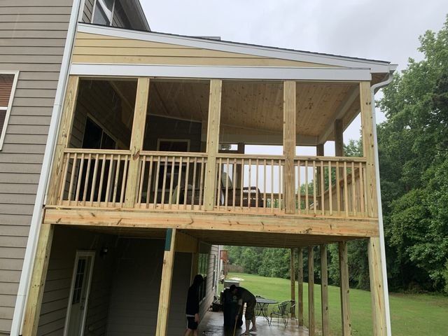 A wooden screened porch built onto the back of a house, with a deck below.  It has a railing and light-colored walls.