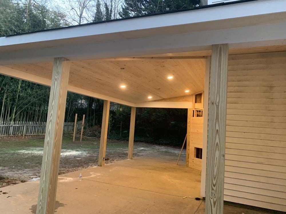 A newly built carport with concrete floor, wooden posts, and recessed lighting. 