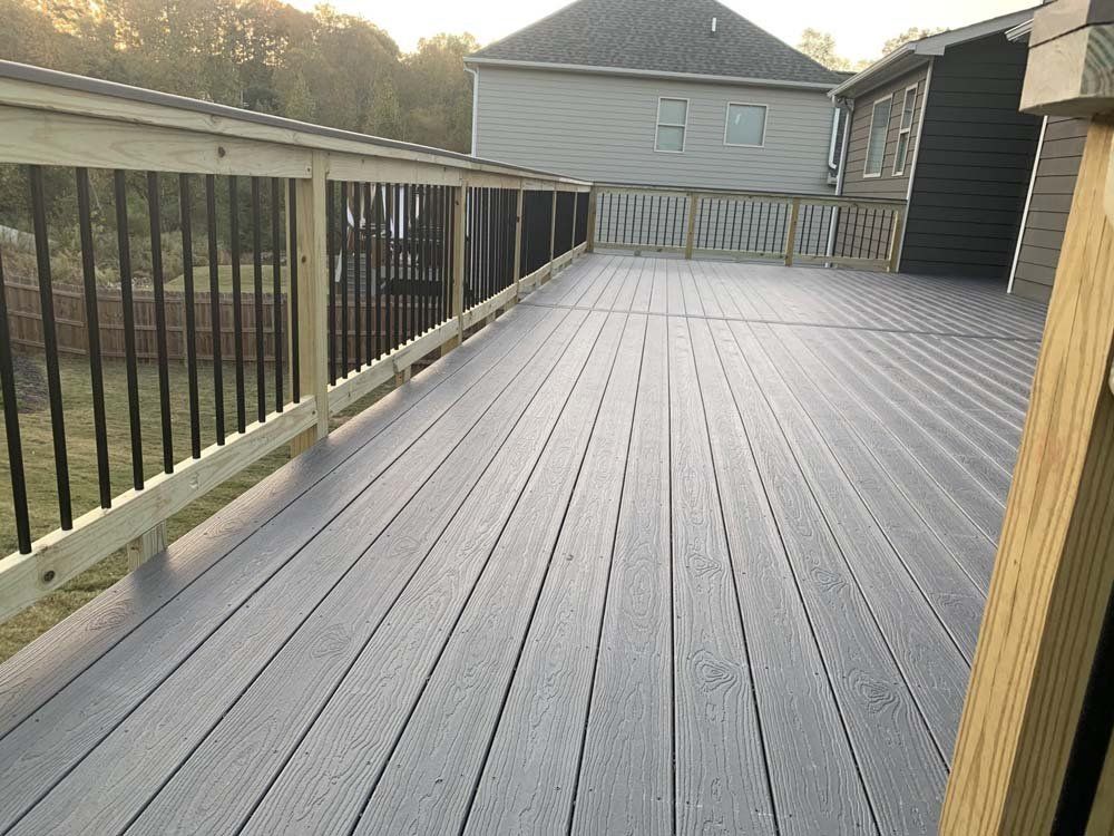 A large gray composite deck with black railings, adjacent to a house.