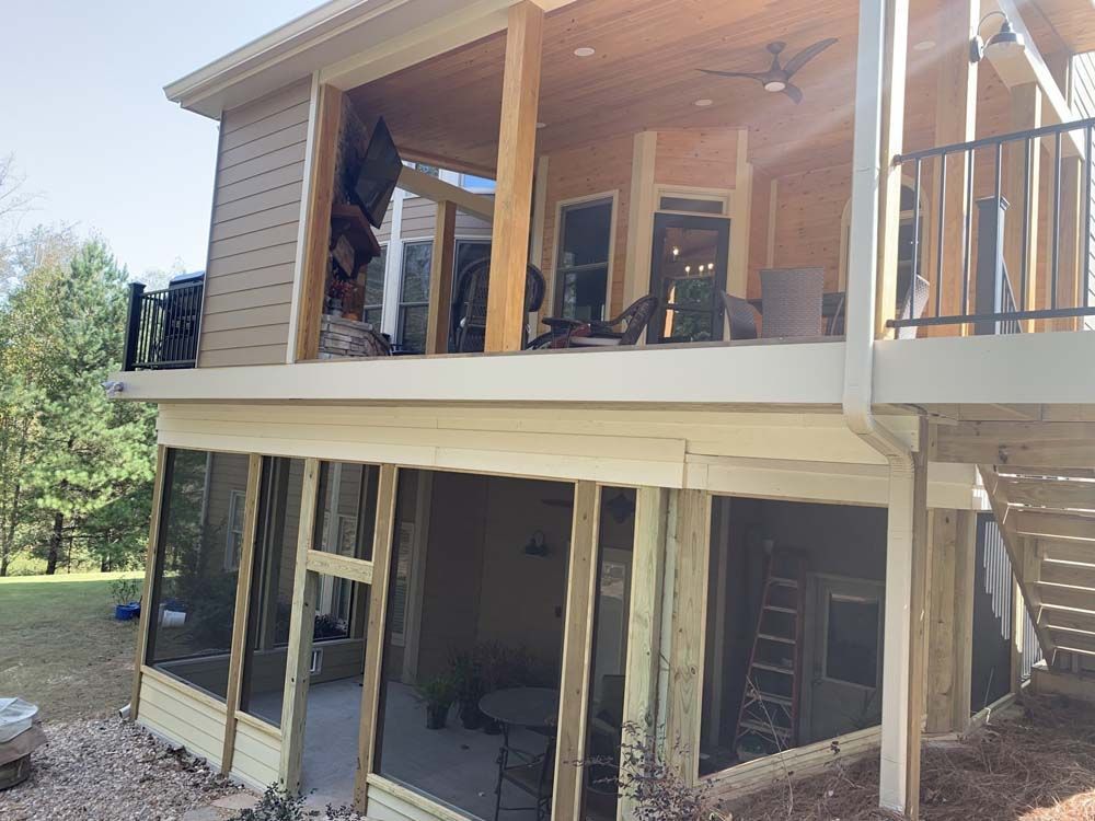 A two-story house with an open-air deck and a screened-in porch. The deck is beige with a black railing